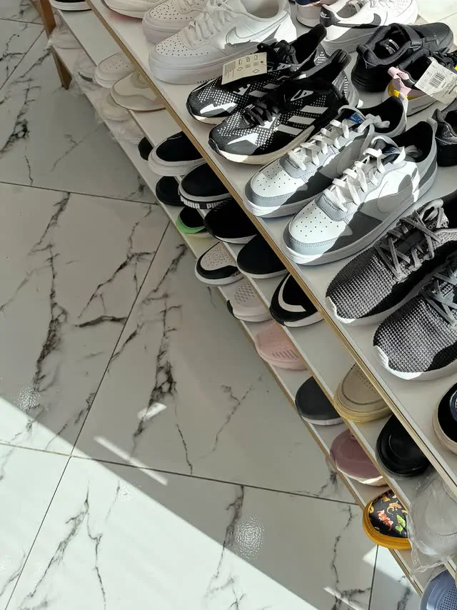 A long white shelf of children's sneakers on the marble floor
